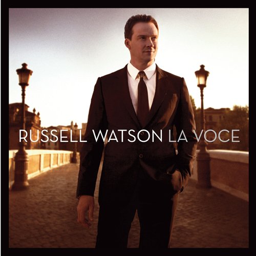 Russell Watson standing on a bridge at sunset with streetlamps, album cover for La Voce.