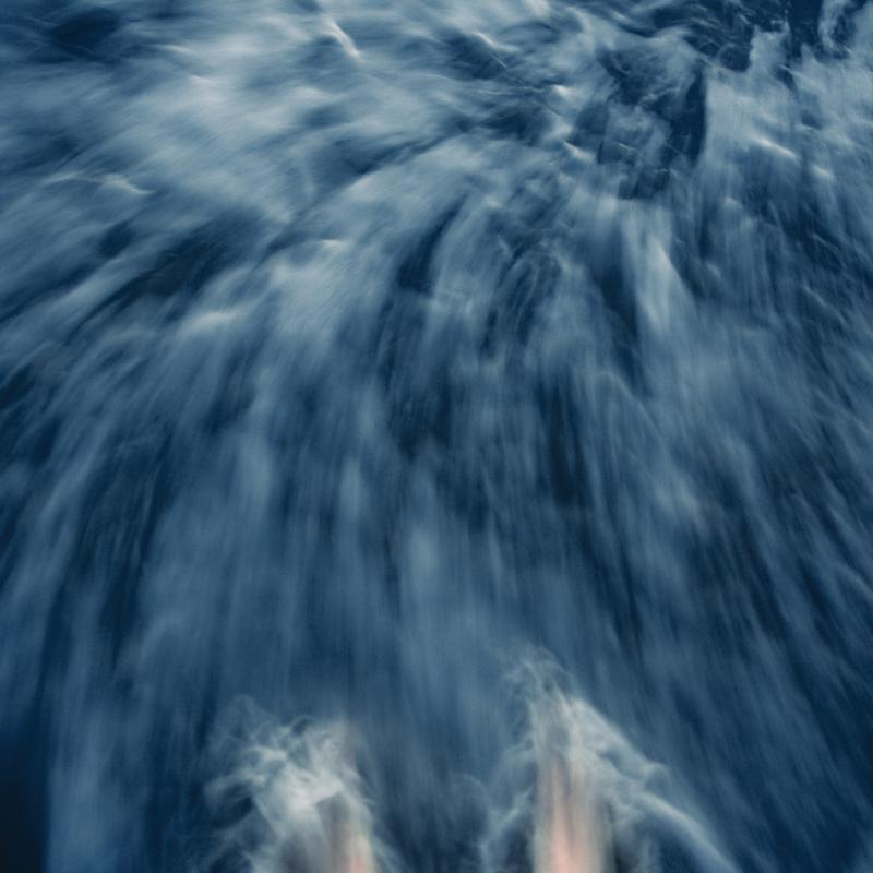 Abstract motion blur of blue and white water with two feet at the bottom.