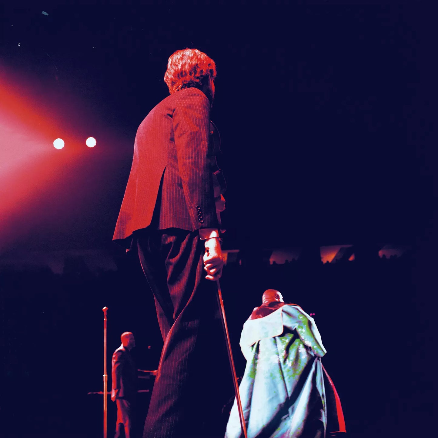 Man with microphone performing on stage with band members.