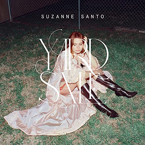 Woman in dress and boots sitting on grass, album cover.