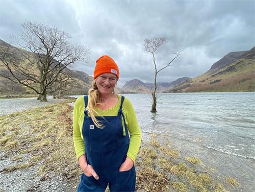 Woman in orange hat stands by a lake and mountains.