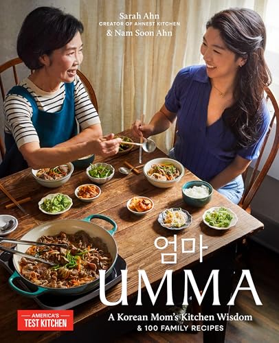 Two women sit at a wooden table sharing a Korean meal with various side dishes.