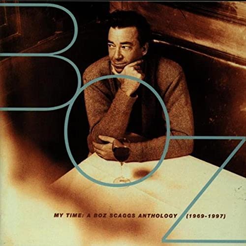 Boz Scaggs sits at a table with a wine glass, overlaid by large blue letters.