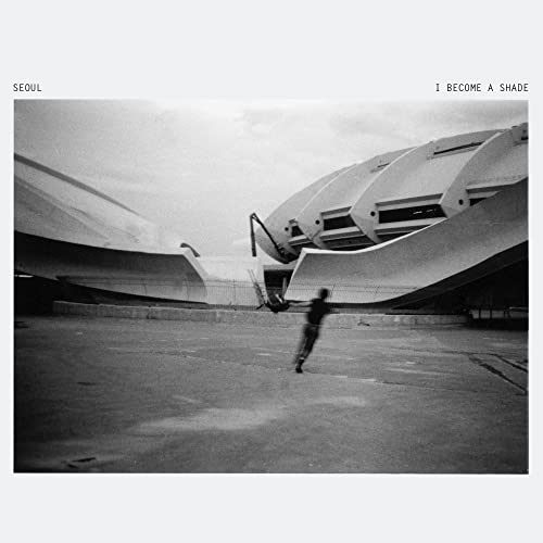 Black and white album cover featuring a building and blurry figure.