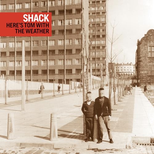 Two children with paper bags over their heads stand before a tall apartment building.