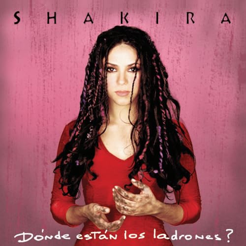 Shakira with dark braided hair and dirty hands wearing a red top, pink background.