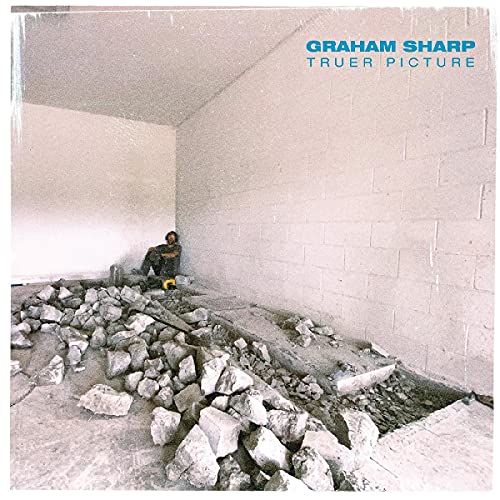Man sitting on rubble in a room with a concrete floor and brick wall.