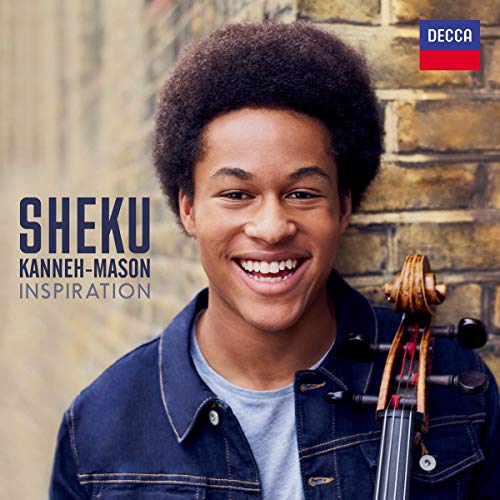 Sheku Kanneh-Mason smiling, holding a cello, against a brick wall background.