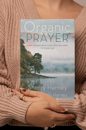 Book cover with a lakeside landscape, held by a person in a sweater.