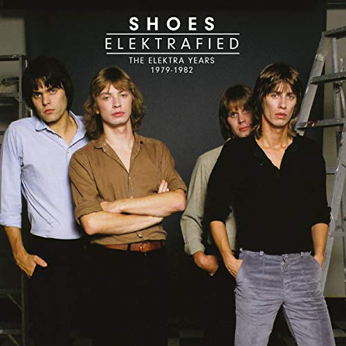 Four band members stand in front of a dark background with ladders on sides.
