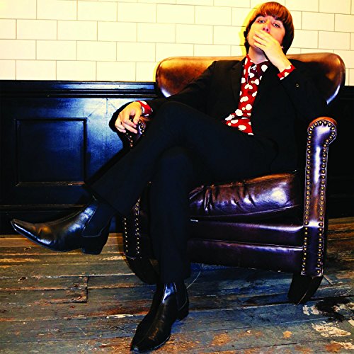 Man in suit and red shirt sits in a brown leather chair.
