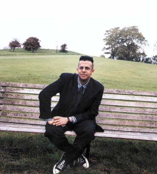 A man in a suit and sneakers sits on a park bench outdoors.