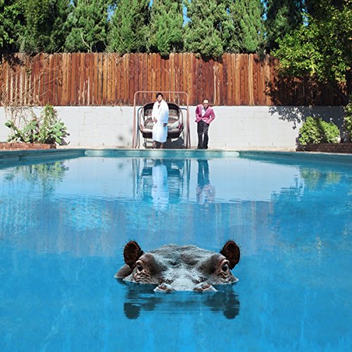 Hippopotamus partially submerged in a swimming pool with two people standing nearby.