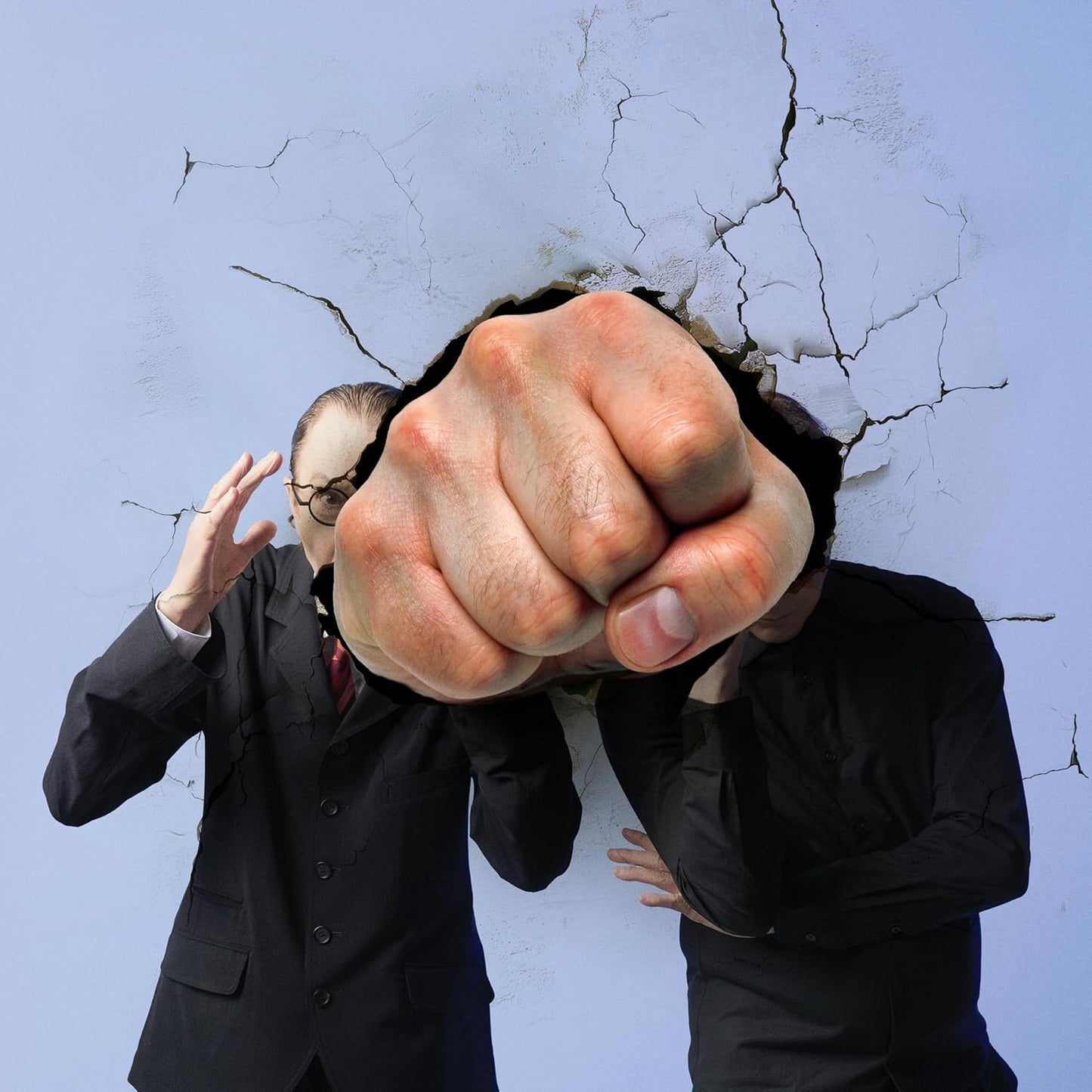 Man in suit with fist breaking through cracked wall.