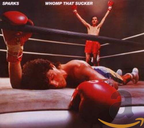 A boxer lies on the mat while another celebrates victory in a boxing ring.