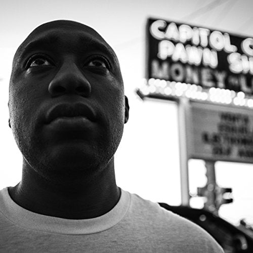 The alt text for the image is: "Black and white portrait of a man in front of a sign."