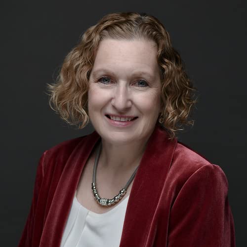 Portrait of a smiling woman with curly red hair wearing a jacket.
