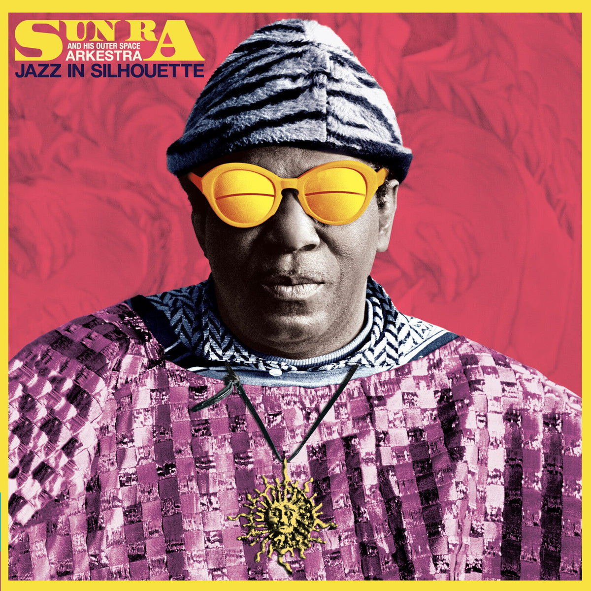 Sun Ra wearing a patterned cap and yellow sunglasses against a red background.