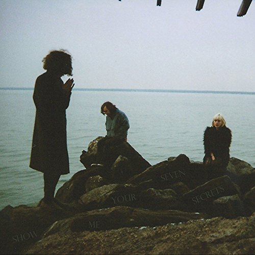 "Album cover featuring three silhouetted figures on rocks by a body of water."