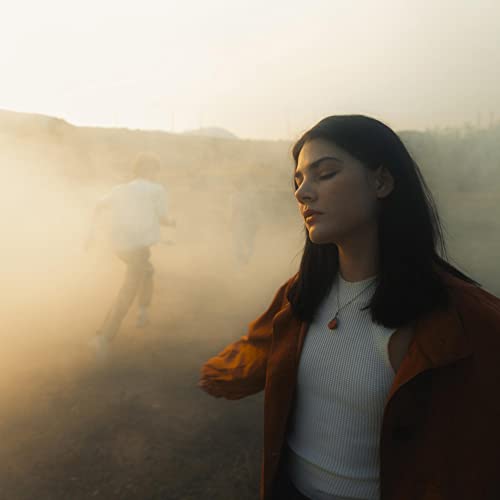 A woman with eyes closed stands in the foreground as a person runs through fog.