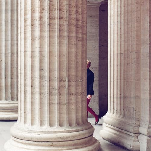 Woman in red pants walking between large, fluted columns.