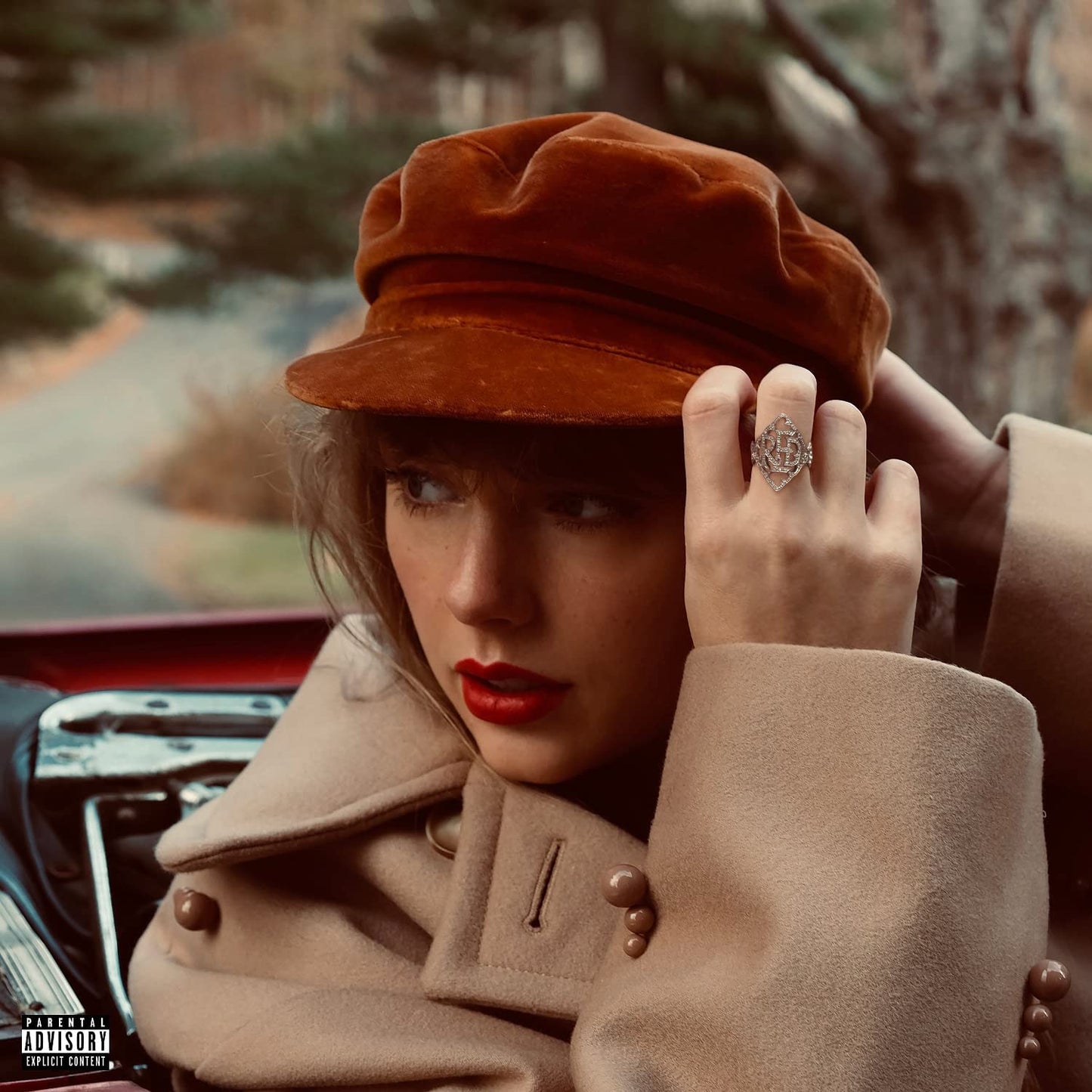 Taylor Swift wearing a brown velvet cap and tan coat with red lipstick.