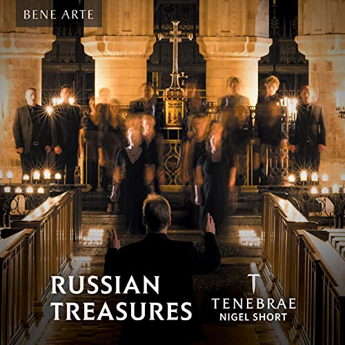 A conductor leads a choir in a dimly lit church with candles and stone pillars.