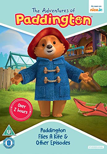Paddington Bear wearing his signature red hat and blue coat stands in a garden.