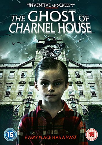 A young boy in a plaid shirt stands before a dark, ominous, old building.