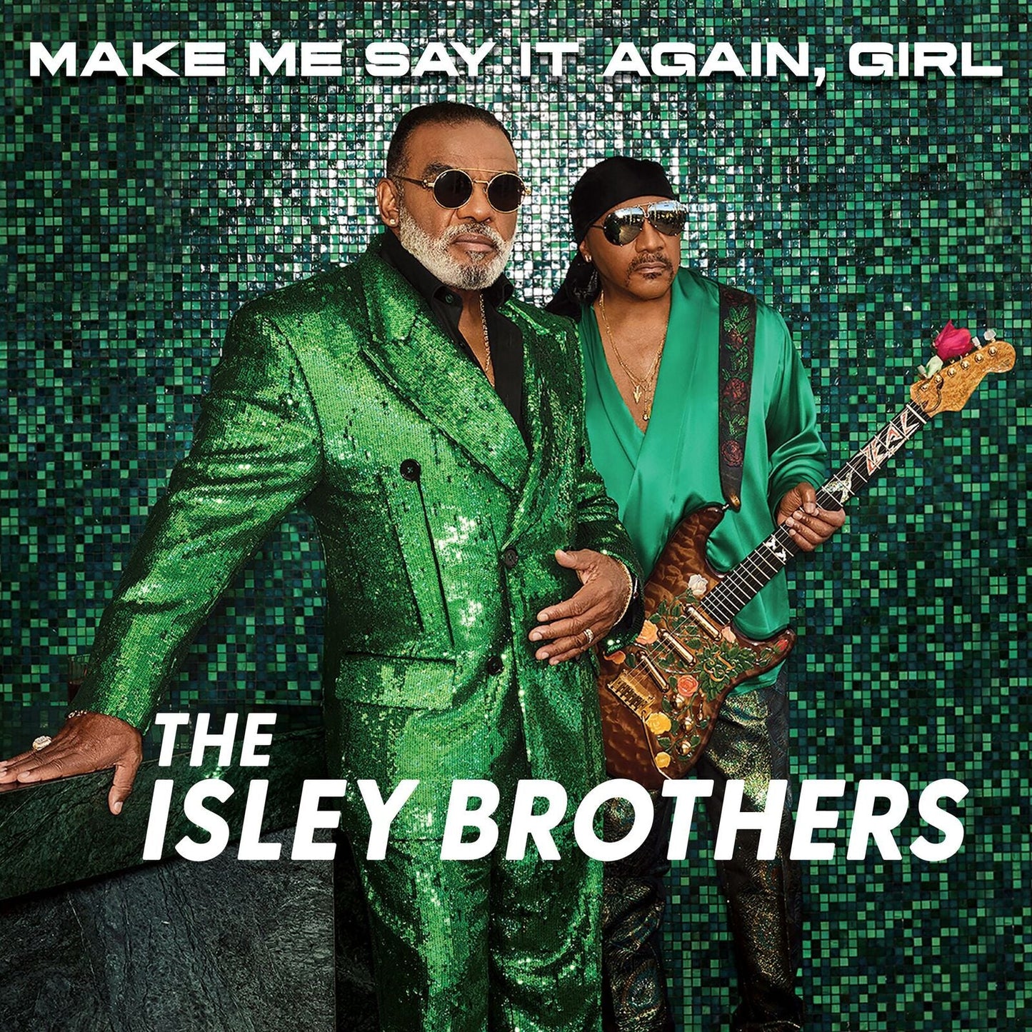 The Isley Brothers wearing green outfits against a green tiled background with an electric guitar.