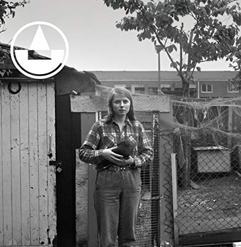 Black and white photo of a woman holding a bird in front of a shed.