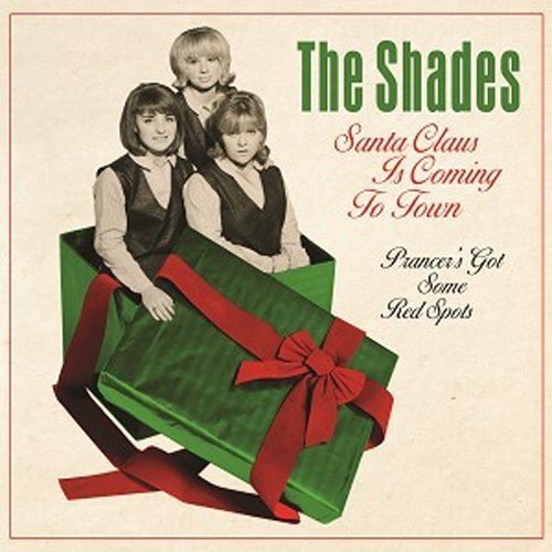 Three women posing inside a large green gift box with a red ribbon.