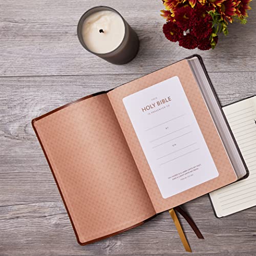 Open brown leather Bible with presentation page, candle, and flowers.