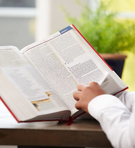 A person's hands turning the pages of an open, multi-column study Bible.
