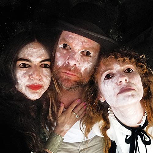 Three people with white face paint pose closely together against a dark background.