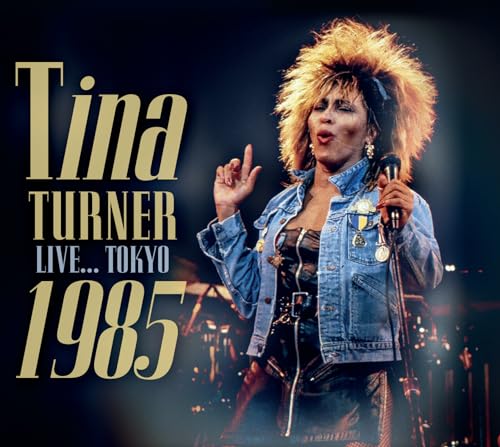 Tina Turner in denim jacket, singing into a microphone onstage.