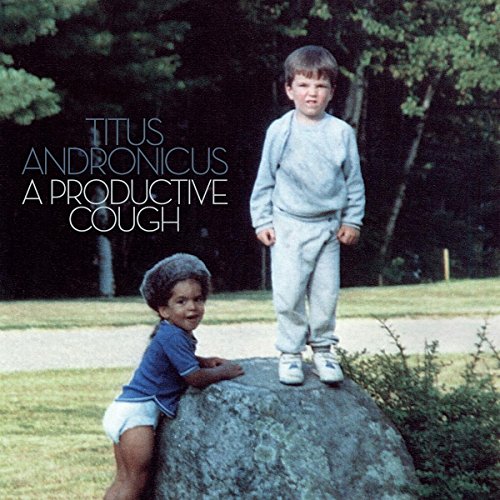 A young boy stands on a rock while a toddler leans against it outdoors.