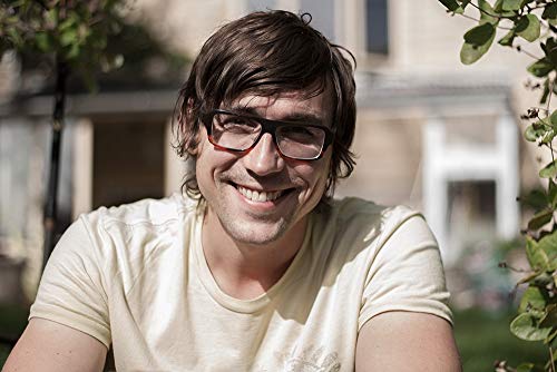 Smiling man with glasses and short brown hair outdoors.