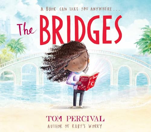 A girl with curly hair stands on a beach reading a book before a bridge.