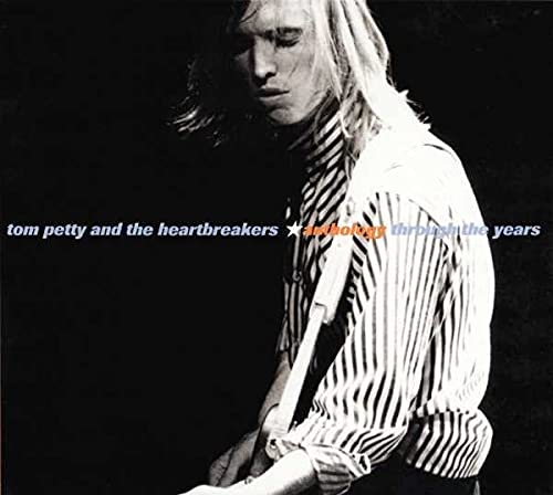 Black and white portrait of Tom Petty wearing a striped shirt while playing guitar.