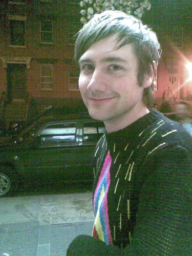 Close-up of a young man with short hair, wearing a colorful sweater.