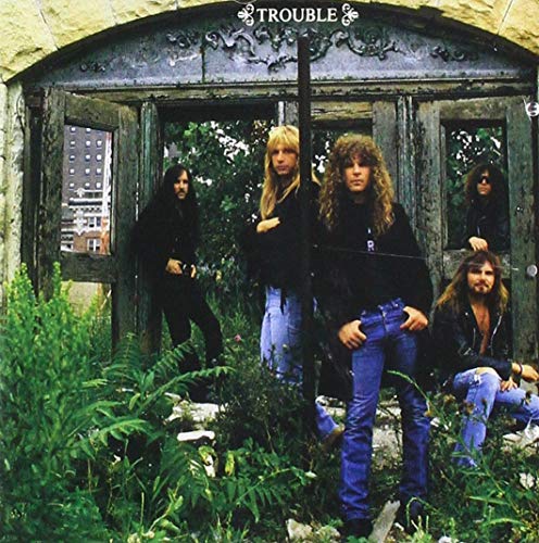 Trouble band members pose in front of a weathered stone doorway.