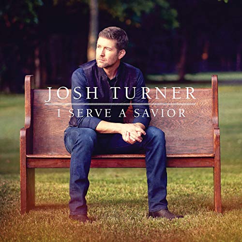 Josh Turner sits on a wooden bench, album cover for “I Serve A Savior.”