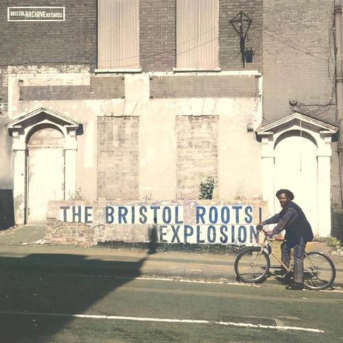 Album cover: man with bicycle in front of a brick building.