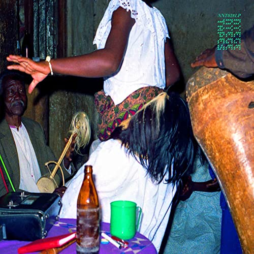 People in traditional clothing play music with drums and a stringed instrument indoors.