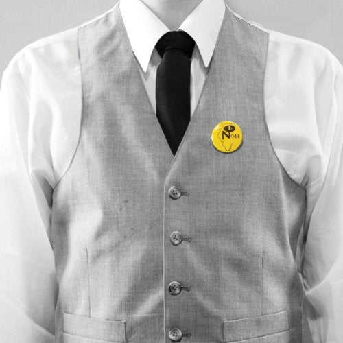 A person in a white shirt and grey vest wearing a yellow button pin.