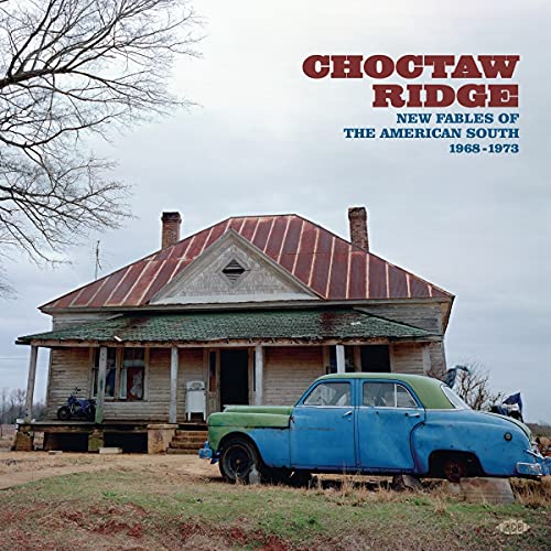 A weathered house with a rusty roof and a blue vintage car parked outside.