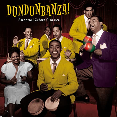 A Cuban musical ensemble in yellow jackets performs on stage with percussion instruments.