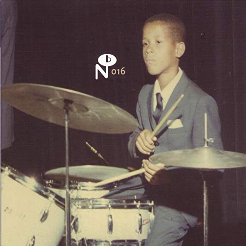 Young drummer in suit stands before a drum kit, sepia tone.