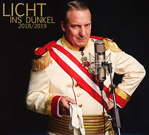 A man in a formal military-style uniform stands before a microphone against black background.